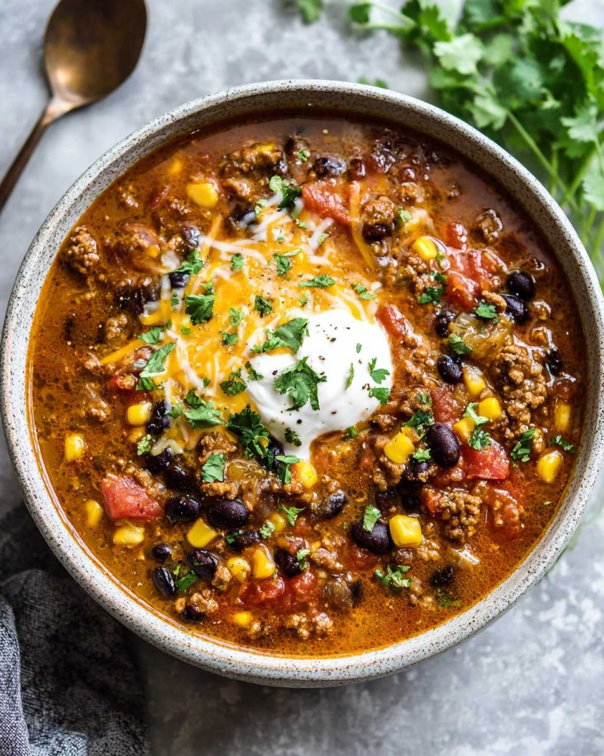 A close-up overhead view of a steaming bowl of Creamy Cowboy Soup, topped with sour cream, shredded cheese, and cilantro.