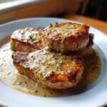 Close-up of three juicy creamy garlic parmesan pork chops smothered in a rich sauce, garnished with herbs.
