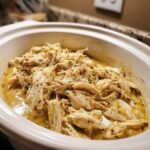Close-up of shredded chicken in a creamy ranch sauce within a white crockpot, perfect for Creamy Ranch Chicken Crockpot.