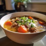 A close-up of a bowl of creamy sausage soup, featuring ground sausage, carrots, and a dollop of sour cream topped with green onions.