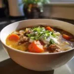 A close-up of a bowl of creamy sausage soup, featuring ground sausage, carrots, and a dollop of sour cream topped with green onions.