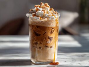 A tall glass of Creme Brulee Iced Coffee topped with whipped cream, caramel drizzle, and cookie crumbles.