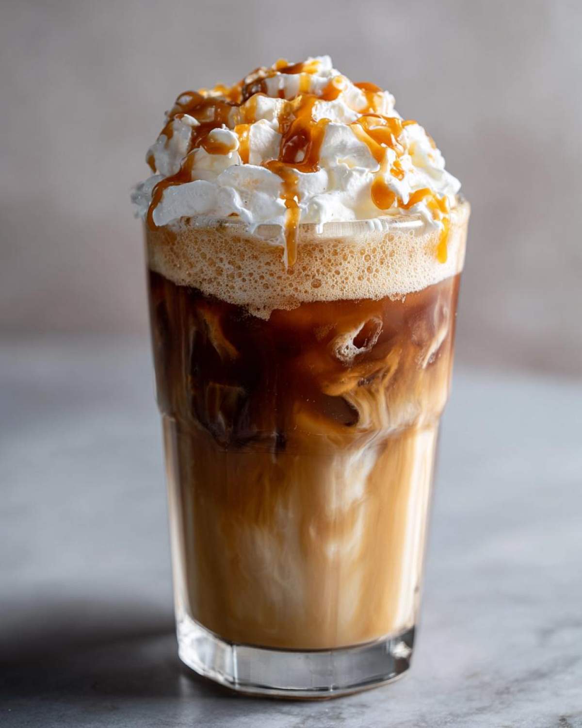A tall glass of Creme Brulee Iced Coffee topped with whipped cream and caramel drizzle.