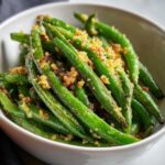 Close-up of a bowl filled with perfectly roasted parmesan green beans, topped with crispy breadcrumbs.