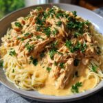 A close-up of Crock Pot Angel Chicken served over spaghetti, generously coated in a creamy, orange-hued sauce and sprinkled with fresh parsley.