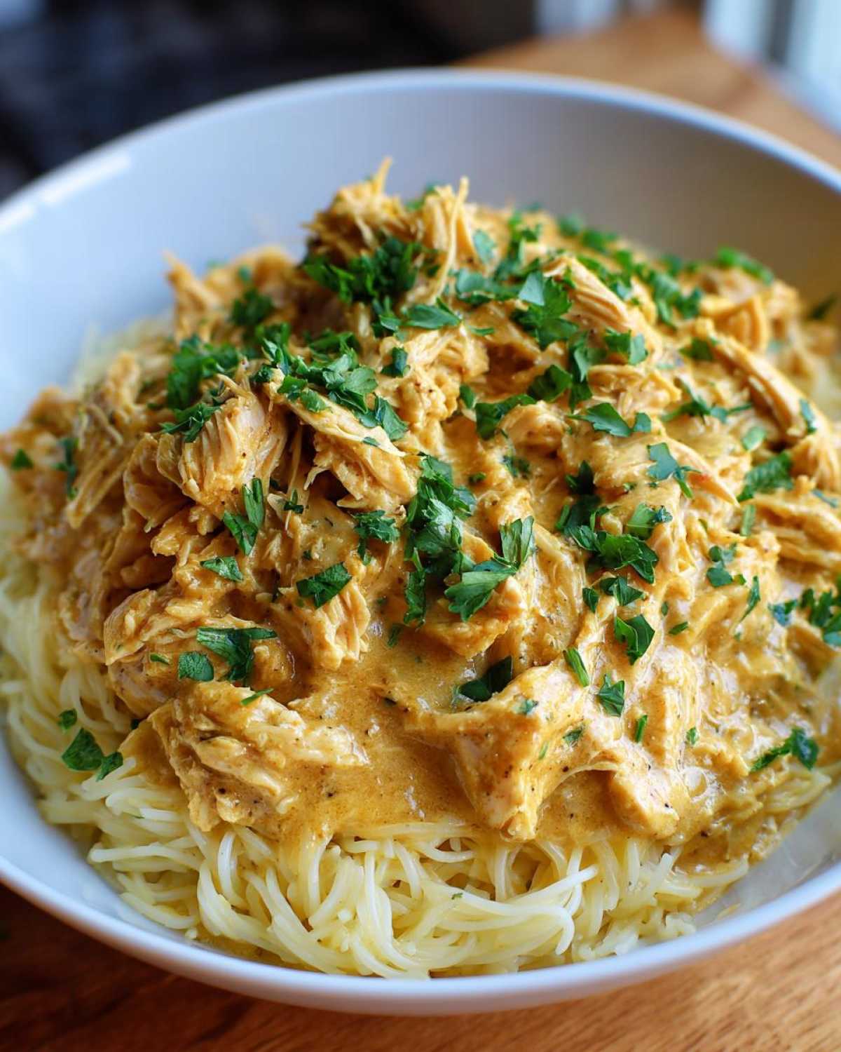 A bowl of spaghetti topped with creamy Crock Pot Angel Chicken and garnished with fresh parsley.