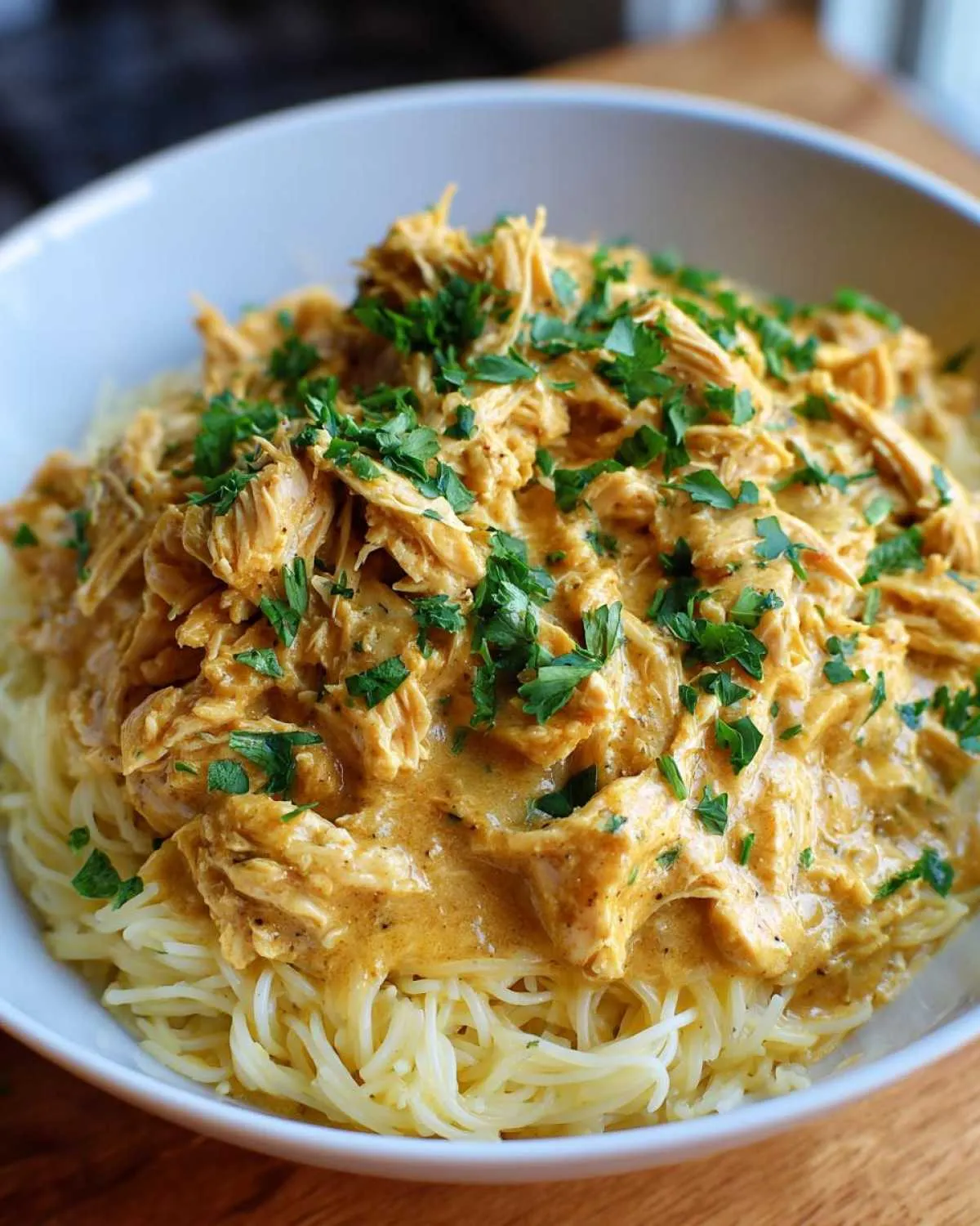 A bowl of spaghetti topped with creamy Crock Pot Angel Chicken and garnished with fresh parsley.