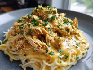 A close-up of Crock Pot Angel Chicken served over pasta and garnished with parsley.