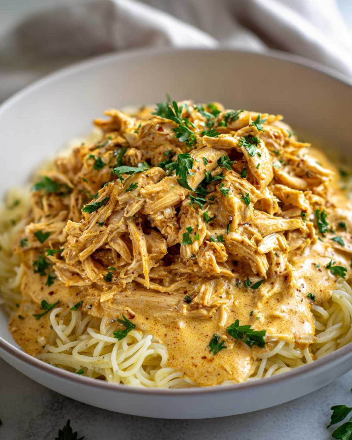 A close-up of Crock Pot Angel Chicken served over spaghetti, topped with fresh parsley.