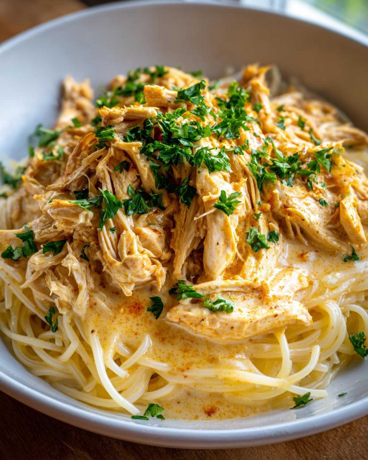 A close-up of Crock Pot Angel Chicken served over a bed of spaghetti, garnished with fresh parsley.