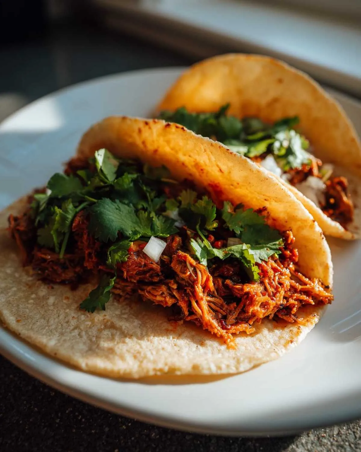 Two delicious crock pot shredded beef tacos filled with tender meat, cilantro, and onions on a white plate.
