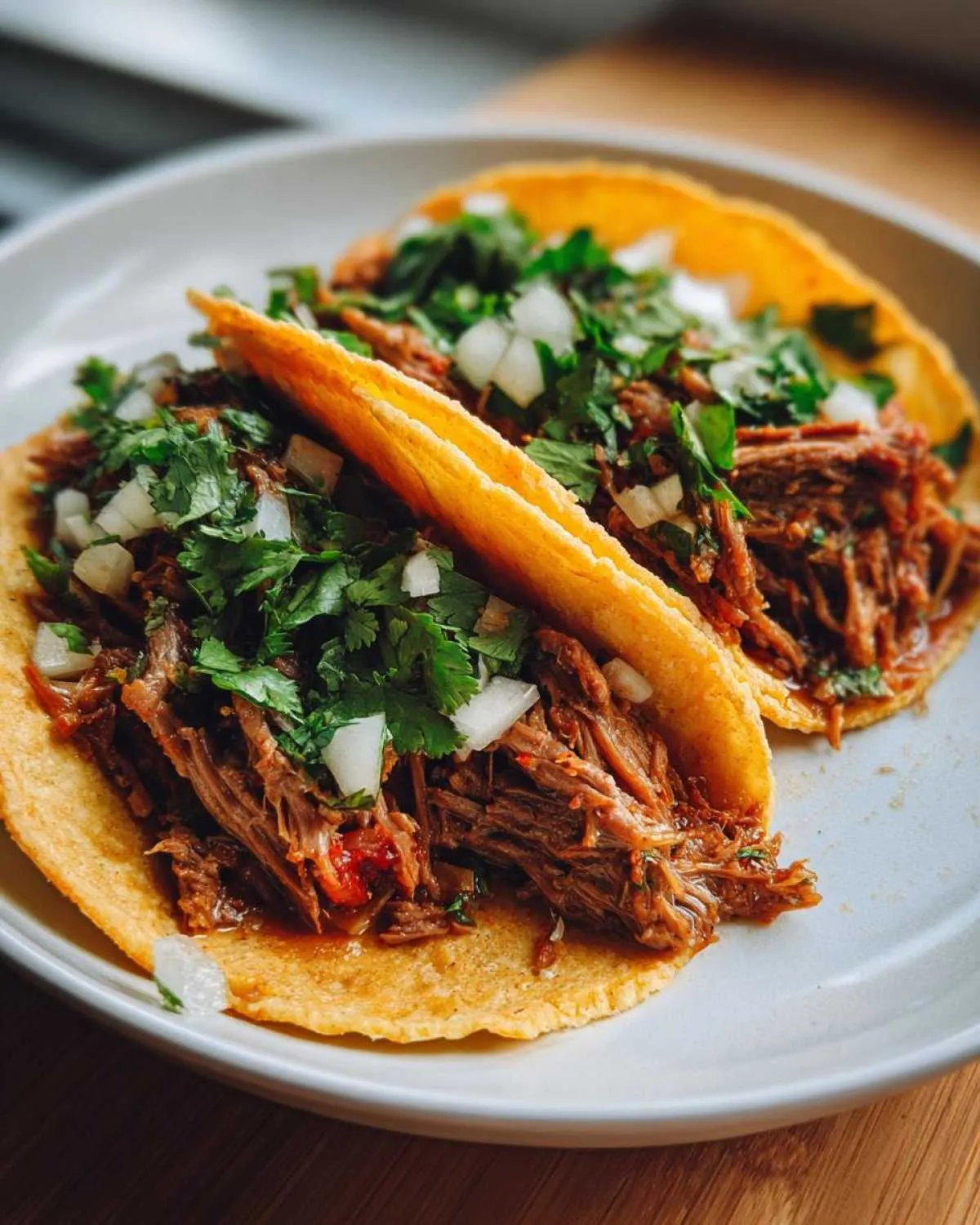 Two delicious crock pot shredded beef tacos filled with tender beef, cilantro, and onions on a white plate.