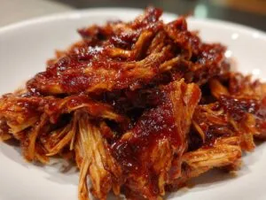 Close-up of shredded crockpot BBQ chicken coated in a rich, glossy sauce.