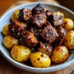 Close-up of Crockpot Garlic Butter Beef Bites with Potatoes in a bowl, glistening with sauce.