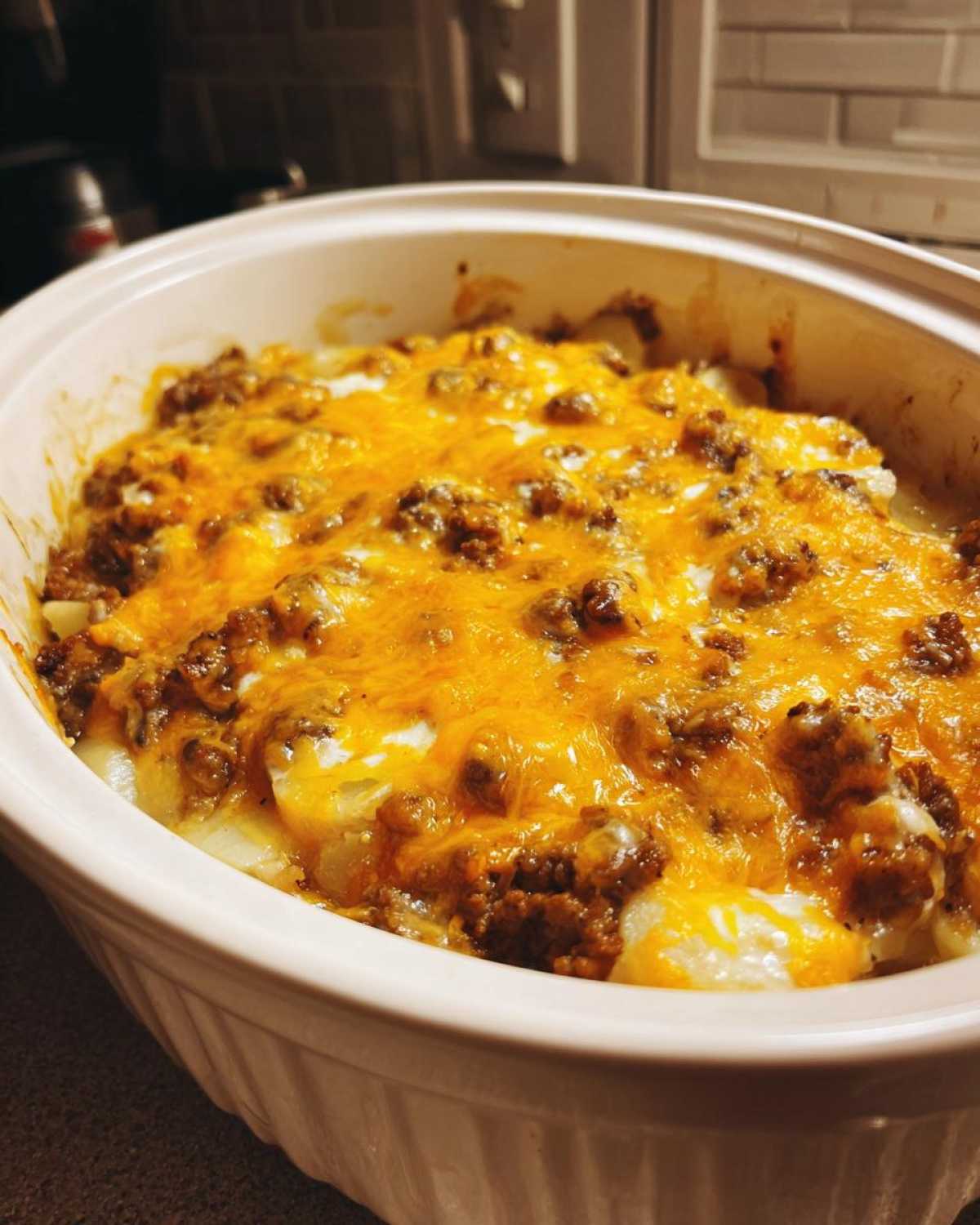 A close-up of a Crockpot hamburger potato casserole topped with melted golden cheese in a white baking dish.