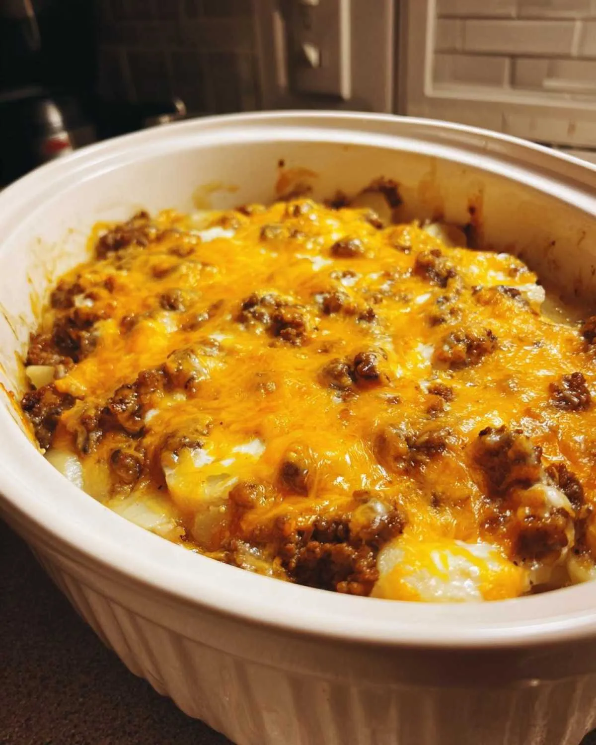 A close-up of a Crockpot hamburger potato casserole topped with melted golden cheese in a white baking dish.