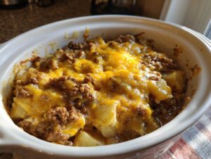 A close-up of a Crockpot hamburger potato casserole topped with melted cheddar cheese, served in a white dish.