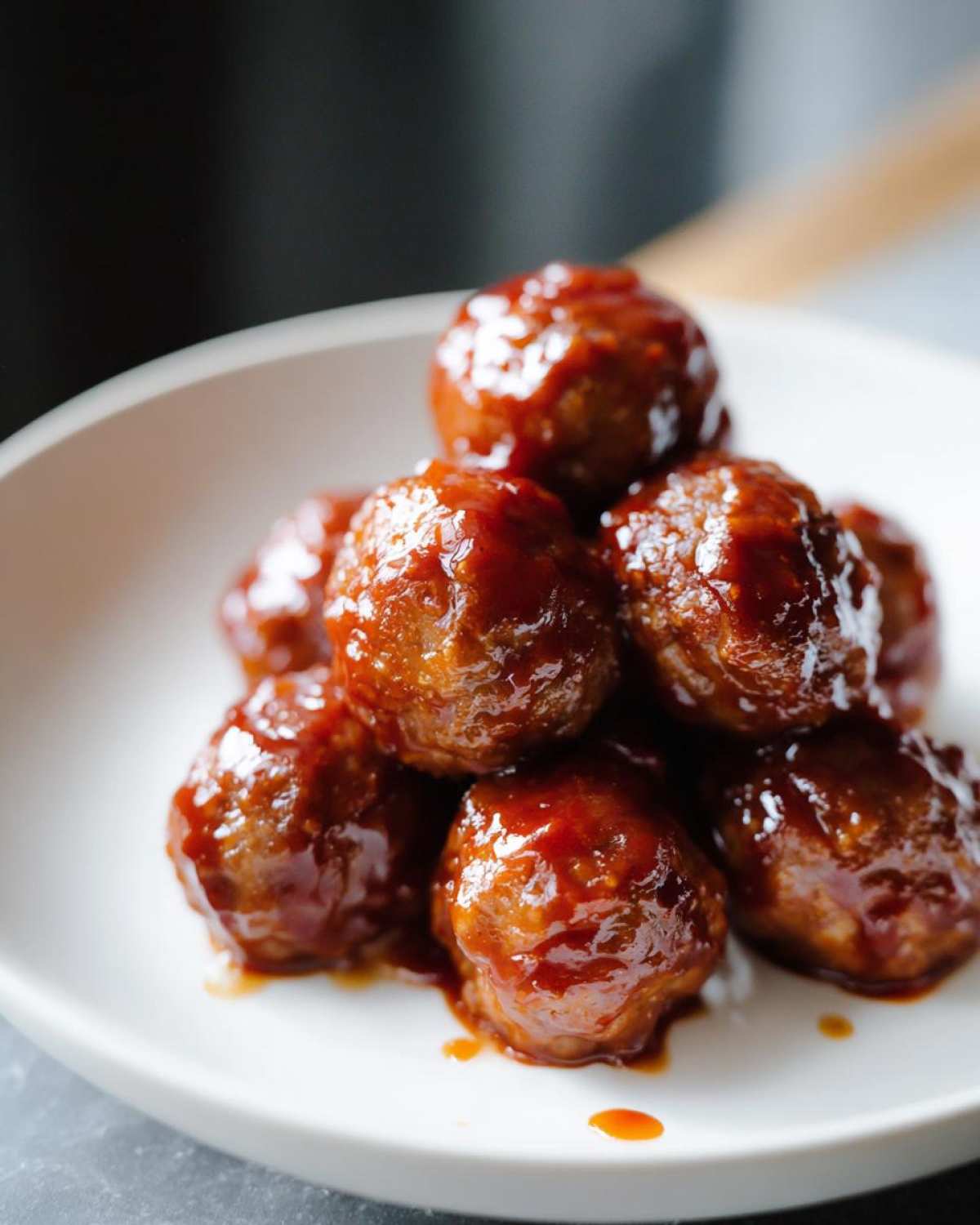 A pile of glossy crockpot sweet chili meatballs coated in a rich, red sauce on a white plate.