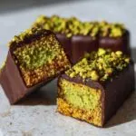 Close-up of a decadent Dubai chocolate bar cut in half, revealing pistachio cream filling and a crunchy base, topped with chopped pistachios.