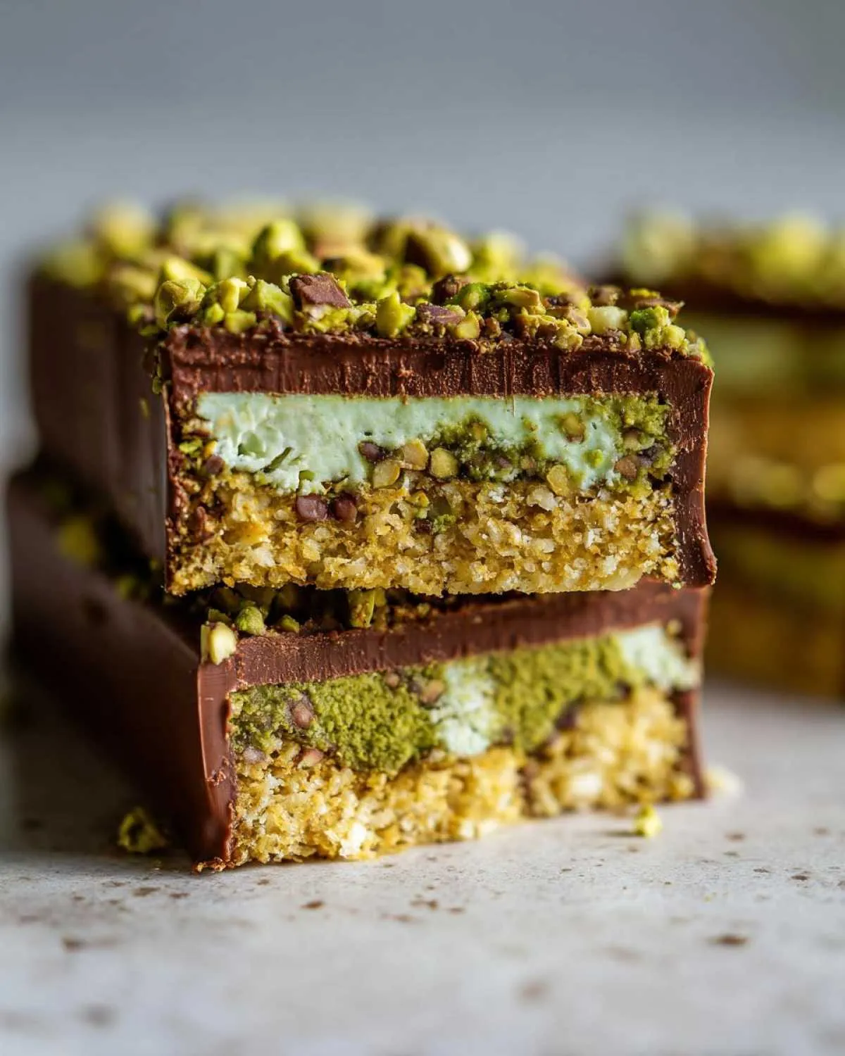 Close-up of stacked Dubai chocolate bars with layers of pistachio cream and crunchy base, topped with chopped pistachios.