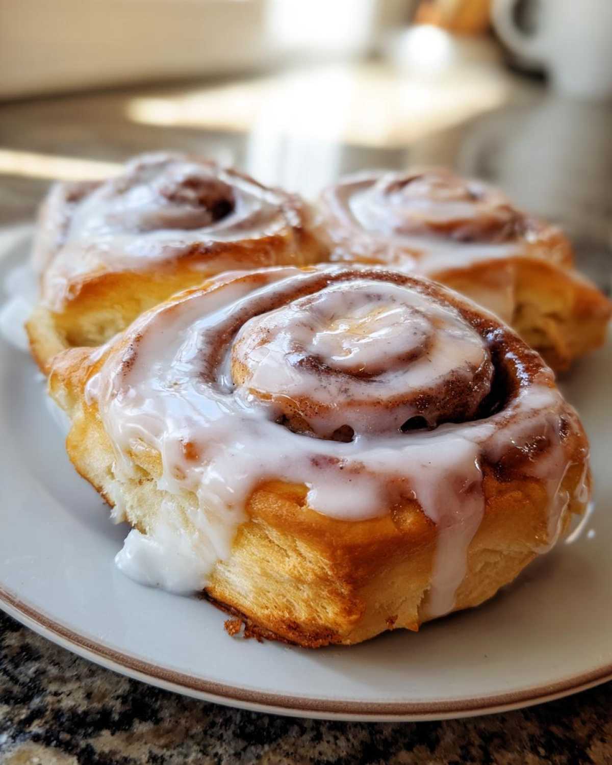 Close-up of three fluffy cinnamon rolls generously topped with a creamy white glaze.