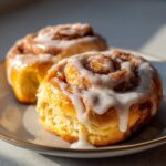 Close-up of two fluffy cinnamon rolls generously drizzled with cream cheese icing on a plate.