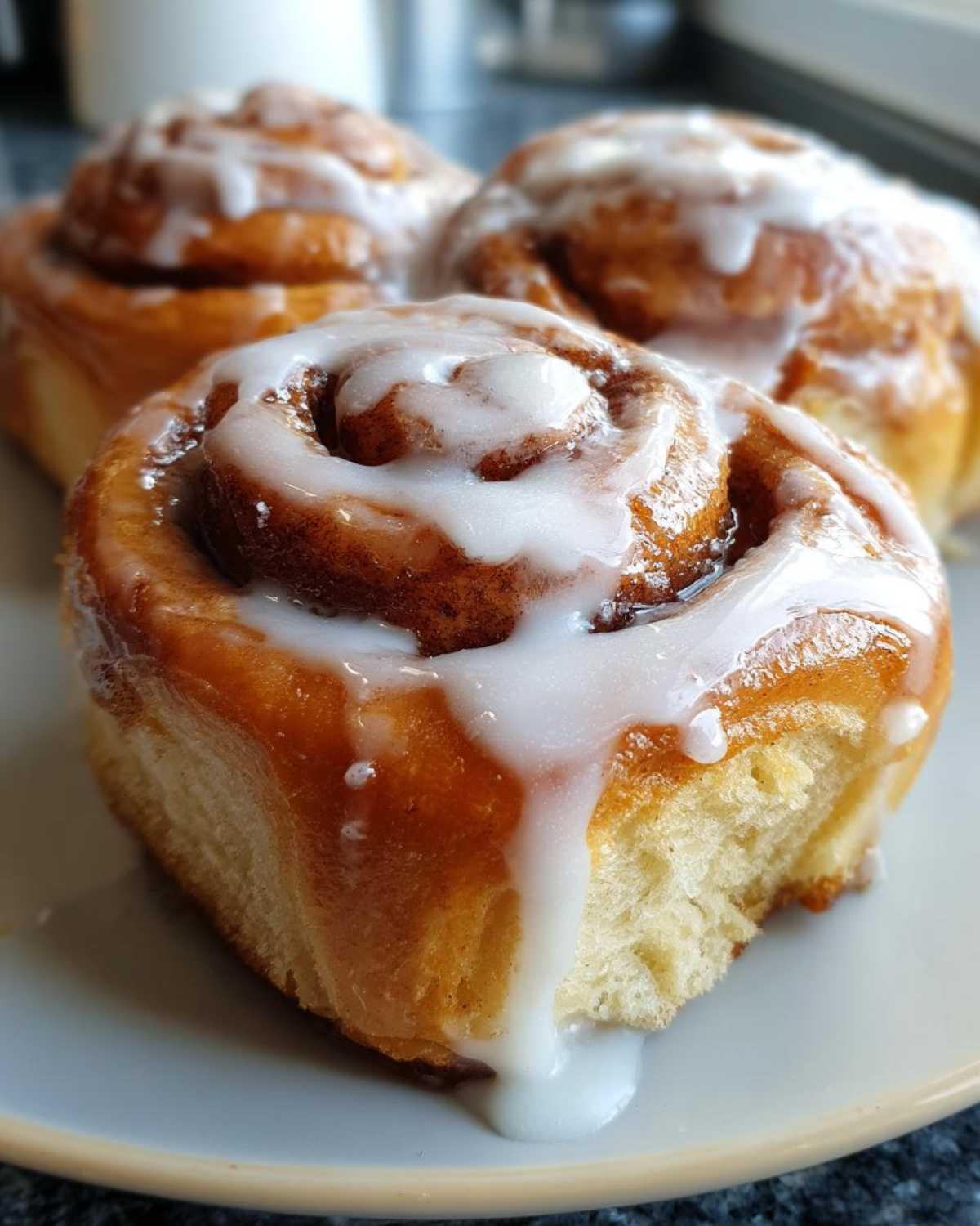 Close-up of fluffy cinnamon rolls topped with drippy cream cheese icing on a plate.