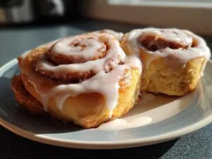 Close-up of two fluffy cinnamon rolls generously topped with white cream cheese icing on a plate.