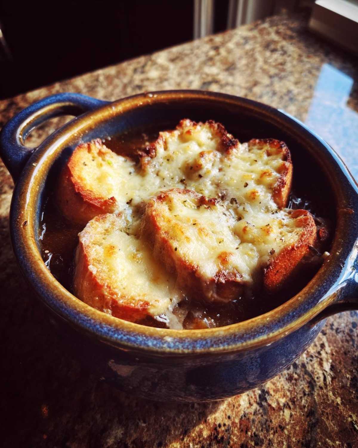 Close-up of French onion beef stew topped with melted cheese and toasted bread.