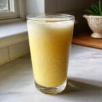 A tall glass filled with frosty, frothy Frozen Creamy Lemonade, perfect for a hot summer day.