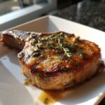 A close-up of a perfectly cooked garlic butter pork chop, glistening with sauce and garnished with fresh thyme.