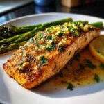 A perfectly cooked fillet of garlic butter salmon served with roasted asparagus and a lemon slice.