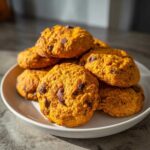 A stack of soft and chewy gluten-free pumpkin cookies loaded with chocolate chips on a white plate.