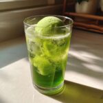 A tall glass filled with bright green Grinch punch and two scoops of lime sherbet, with ice and bubbles.