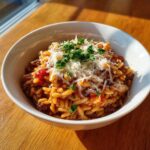 A close-up of a white bowl filled with delicious ground beef orzo, topped with grated cheese and fresh parsley.