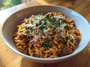 A close-up of a white bowl filled with delicious ground beef orzo, topped with shredded cheese and fresh parsley.