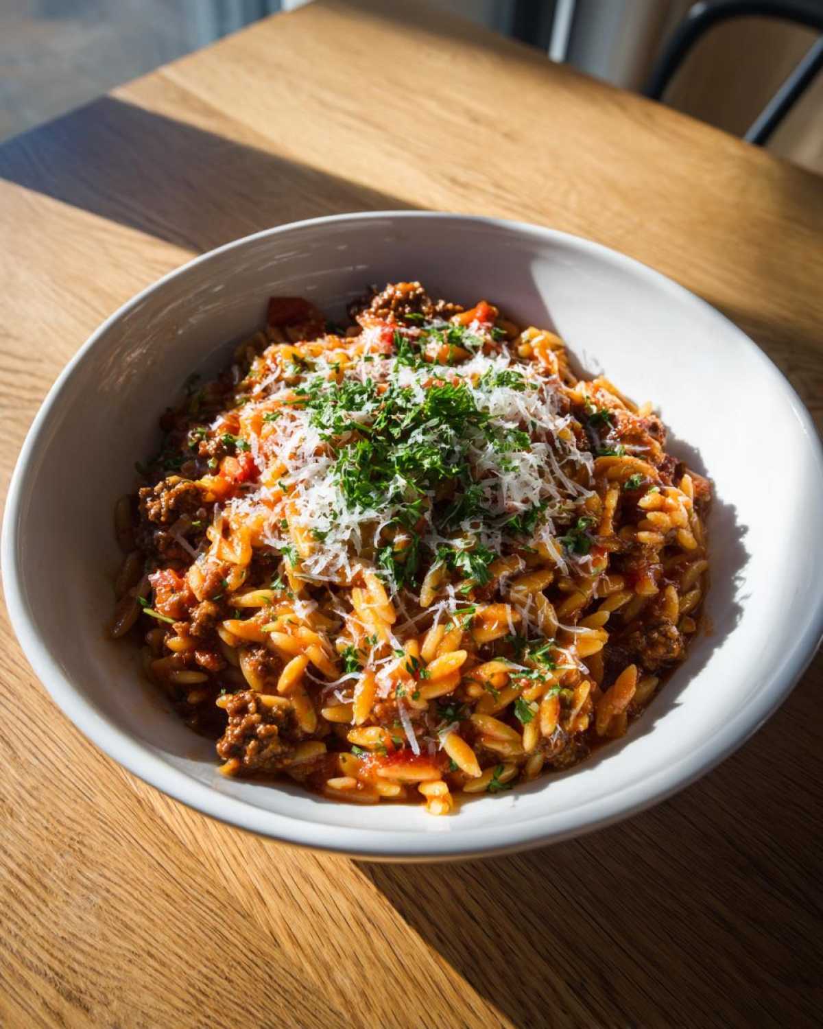 A bowl of delicious ground beef orzo pasta topped with grated cheese and fresh parsley.