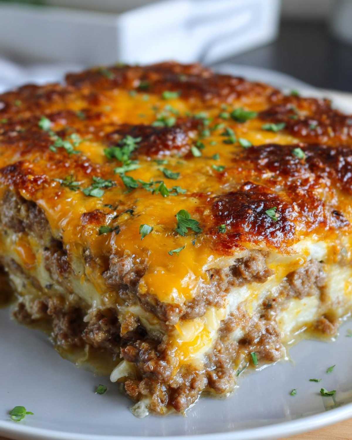 A close-up of a hearty slice of hamburger potato casserole, topped with melted cheese and parsley.