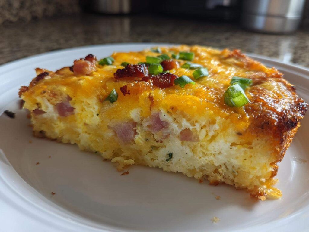 A tempting slice of hash brown egg casserole with ham, melted cheese, and green onions.
