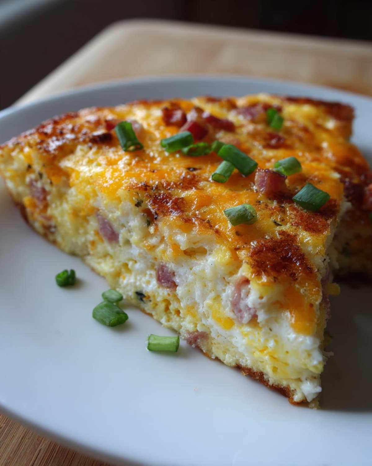 A slice of hash brown egg casserole topped with melted cheese and green onions.