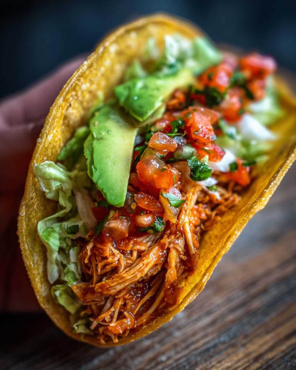 A close-up of a healthy crockpot chicken taco filled with shredded chicken, lettuce, avocado, and pico de gallo.