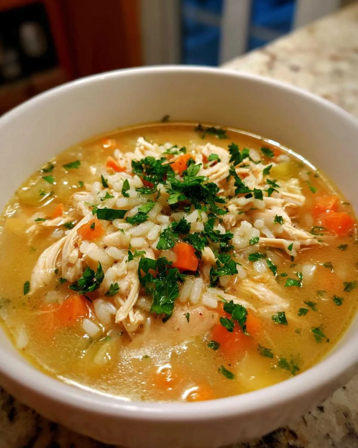 A close-up of a bowl of hearty chicken and rice soup, garnished with fresh parsley.
