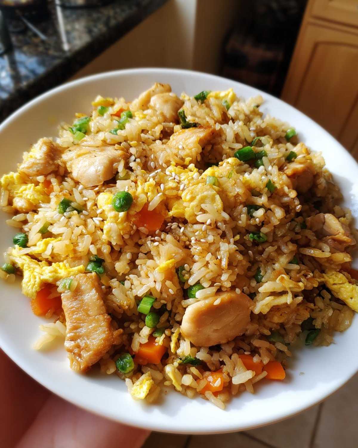 A close-up of a white bowl filled with high protein chicken fried rice, featuring chicken pieces, scrambled eggs, peas, and carrots.