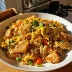 A close-up of a bowl of high protein chicken fried rice, showcasing tender chicken pieces, scrambled eggs, peas, and carrots.