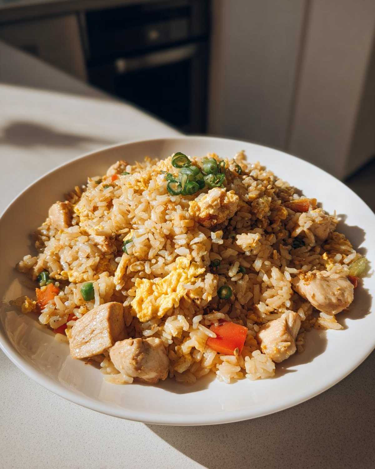 A white bowl filled with high protein chicken fried rice, featuring chunks of chicken, scrambled eggs, peas, and diced carrots.