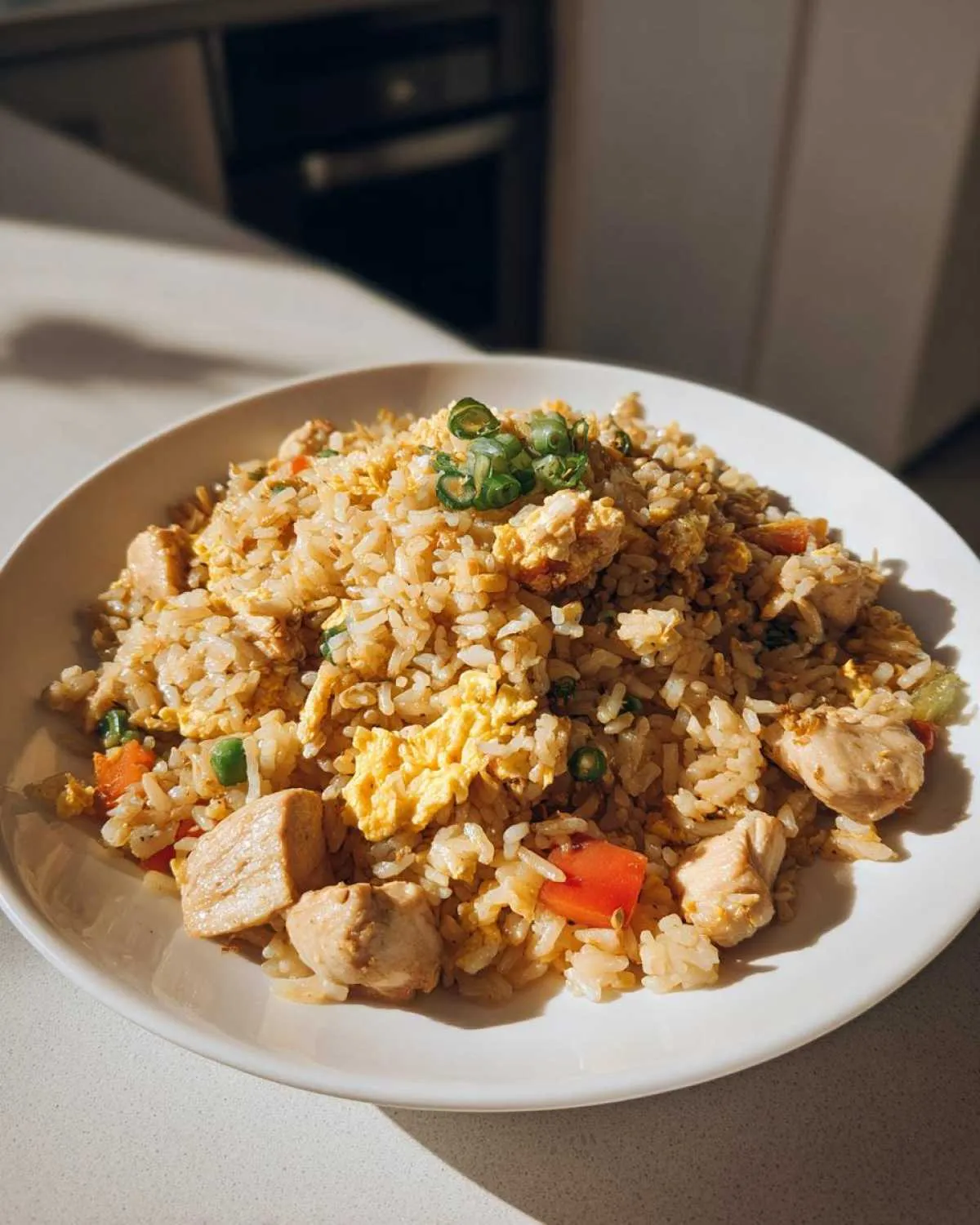 A white bowl filled with high protein chicken fried rice, featuring chunks of chicken, scrambled eggs, peas, and diced carrots.