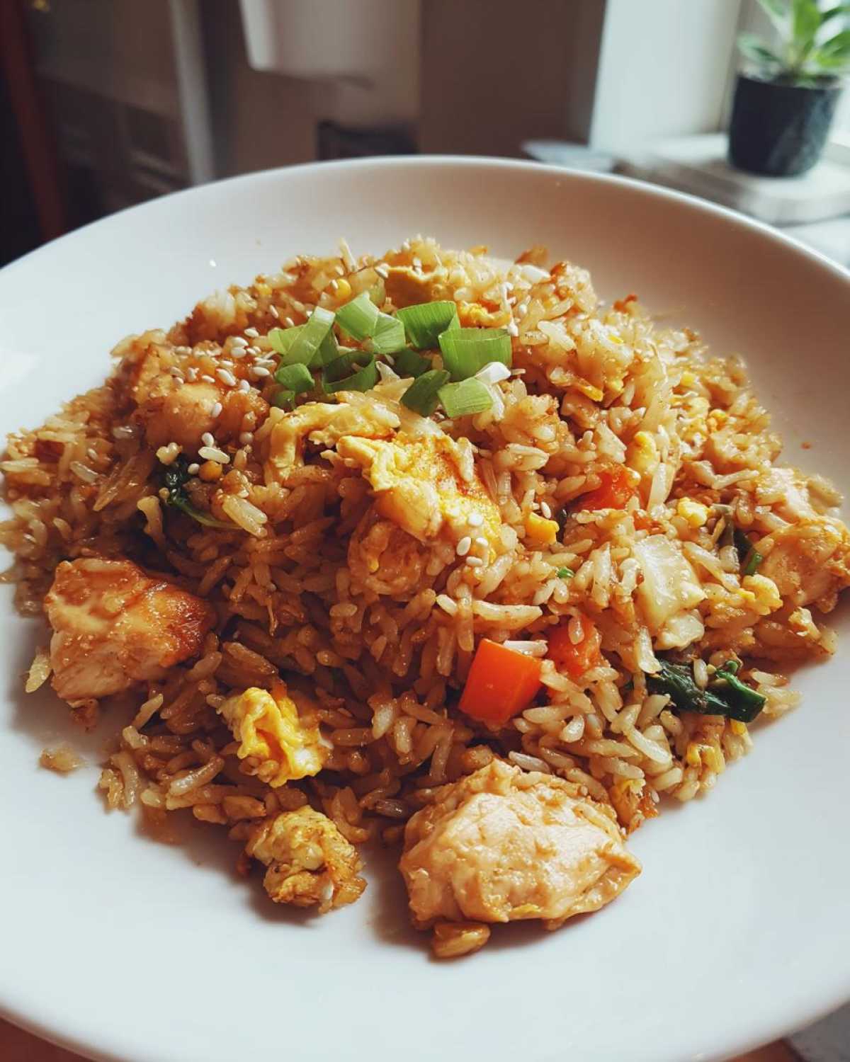 A close-up of a white bowl filled with high protein chicken fried rice, garnished with green onions and sesame seeds.