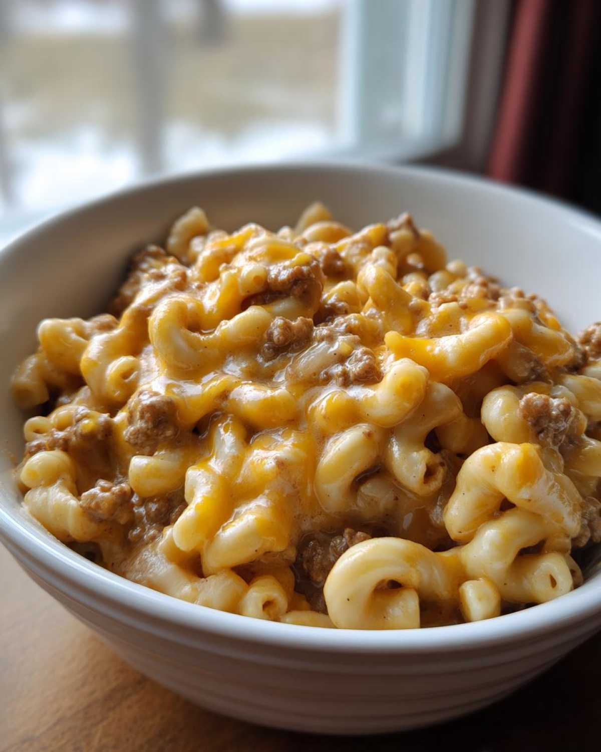 A close-up of a white bowl filled with creamy, cheesy Homemade Hamburger Helper with elbow macaroni and ground beef.