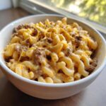 A close-up of a white bowl filled with cheesy homemade hamburger helper, featuring elbow macaroni and seasoned ground beef.