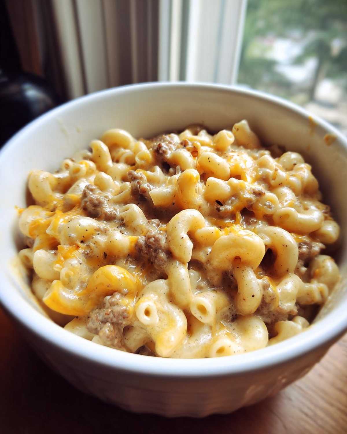 A close-up of a white bowl filled with creamy Homemade Hamburger Helper, featuring elbow macaroni and seasoned ground beef.